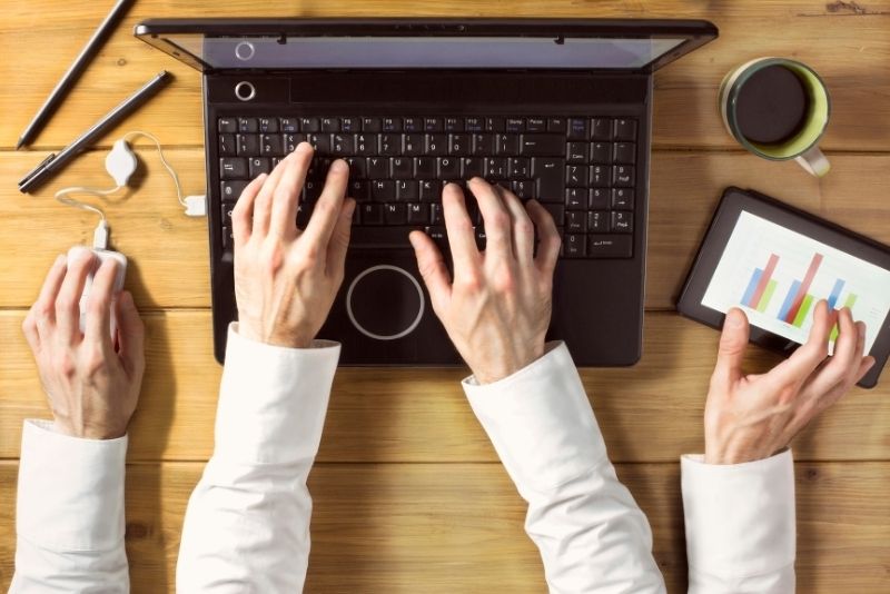 An image of a person sitting at a desk with multiple devices and papers scattered around to depict multitasking.